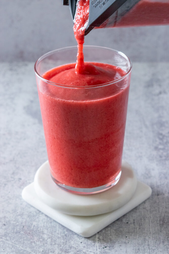 An icy, thick stream of frozen raspberry lemonade being poured from the blender into a glass.