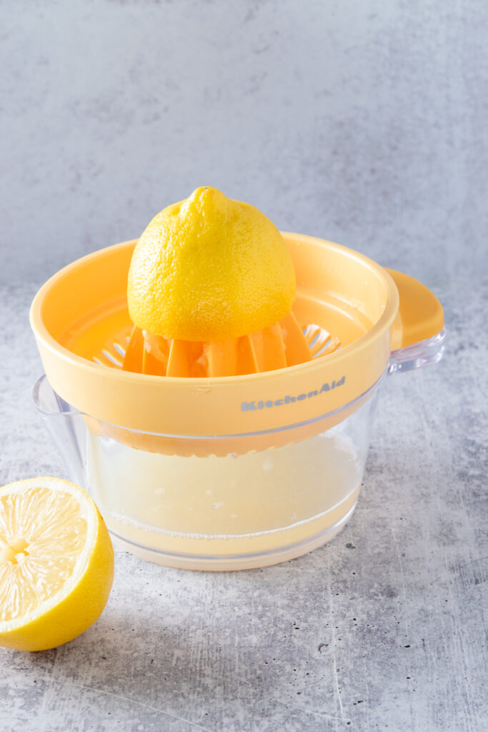 A lemon juicer with half a lemon on it, with the bowl filled with lemon juice.