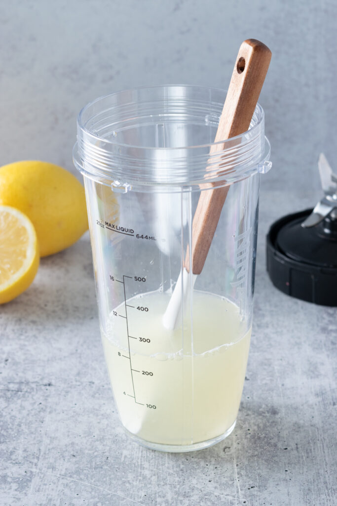 The lemon juice mixture being stirred in blender cup to dissolve the sugar.