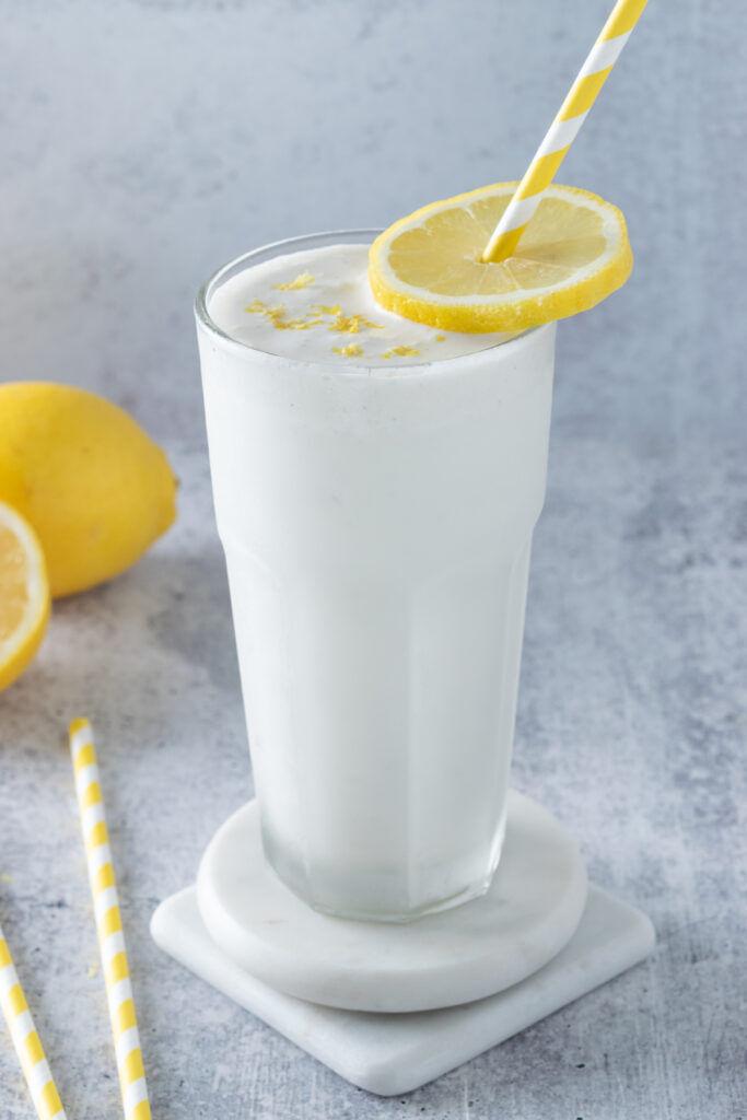 Frosted lemonade poured into a frosty cup that's been chilled in the freezer. The lemonade is topped with zest and a slice of lemon to garnish.
