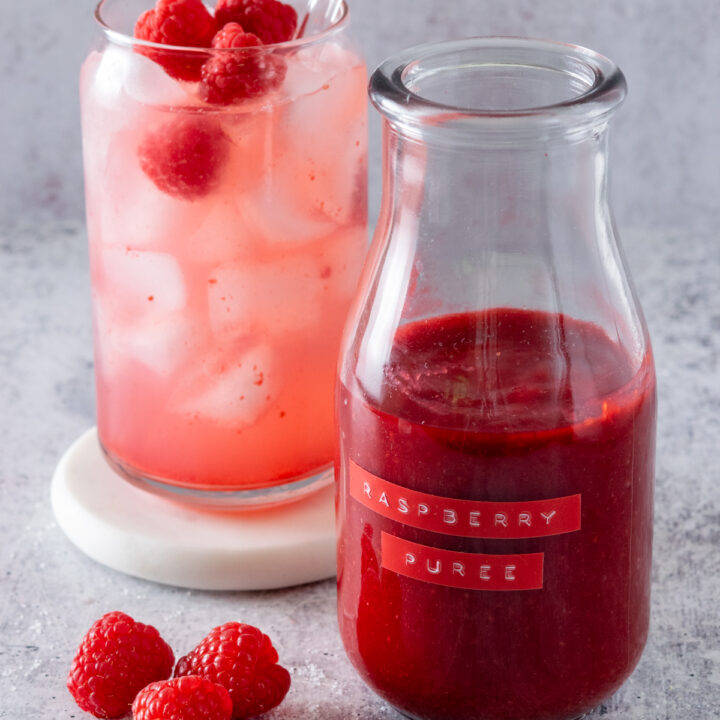 Homemade raspberry puree in a bottle next to a raspberry lemonade drink.