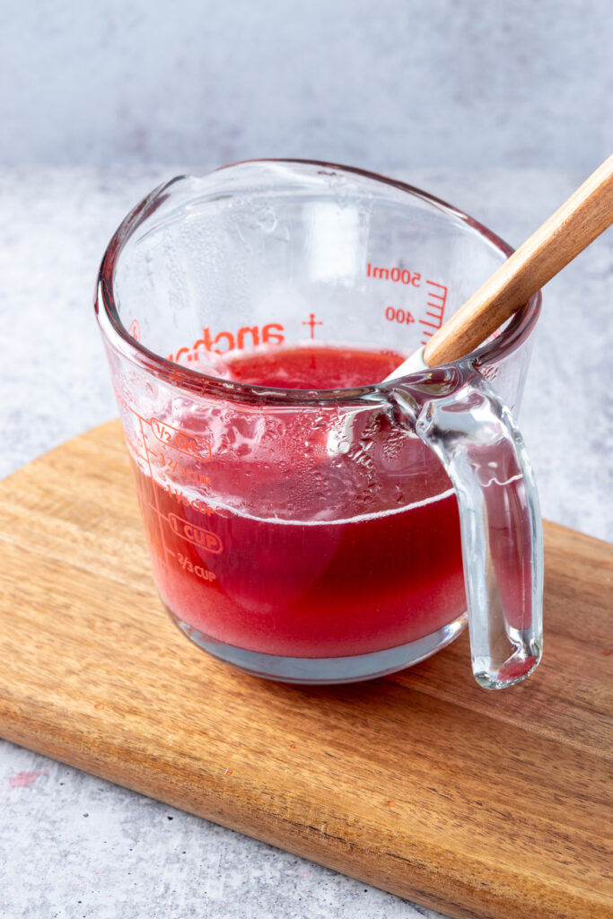 Glass Pyrex measuring cup with raspberry juice and sugar in it.