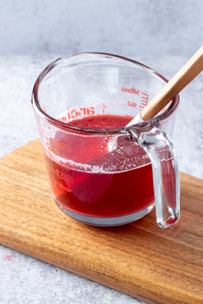 Pyrex glass measuring cup and rubber spatula in it, to stir the sugar into the raspberry juice.