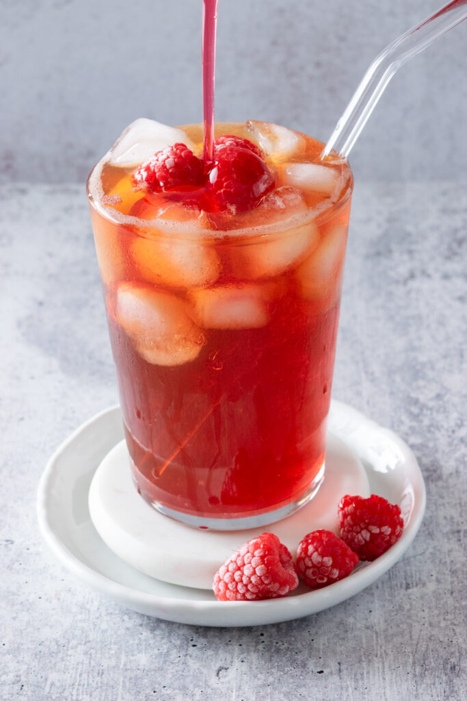 Raspberry syrup being poured into a refreshing glass of iced tea.