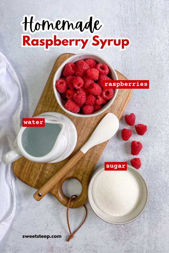 Overhead picture showing the ingredients needed to make homemade raspberry syrup for drinks, including a bowl of fresh raspberries, small pitcher of water and bowl of sugar. The ingredients are on a wooden cutting board next to a white rubber spatula and a few loose raspberries.