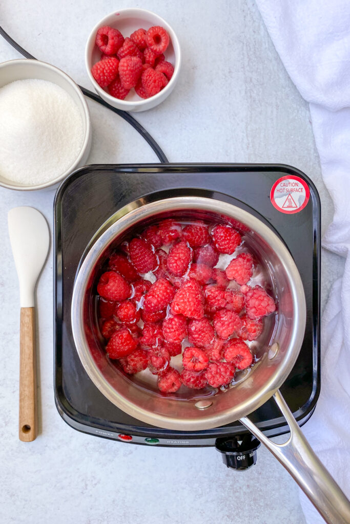 A saucepan with raspberries and water on the stove.