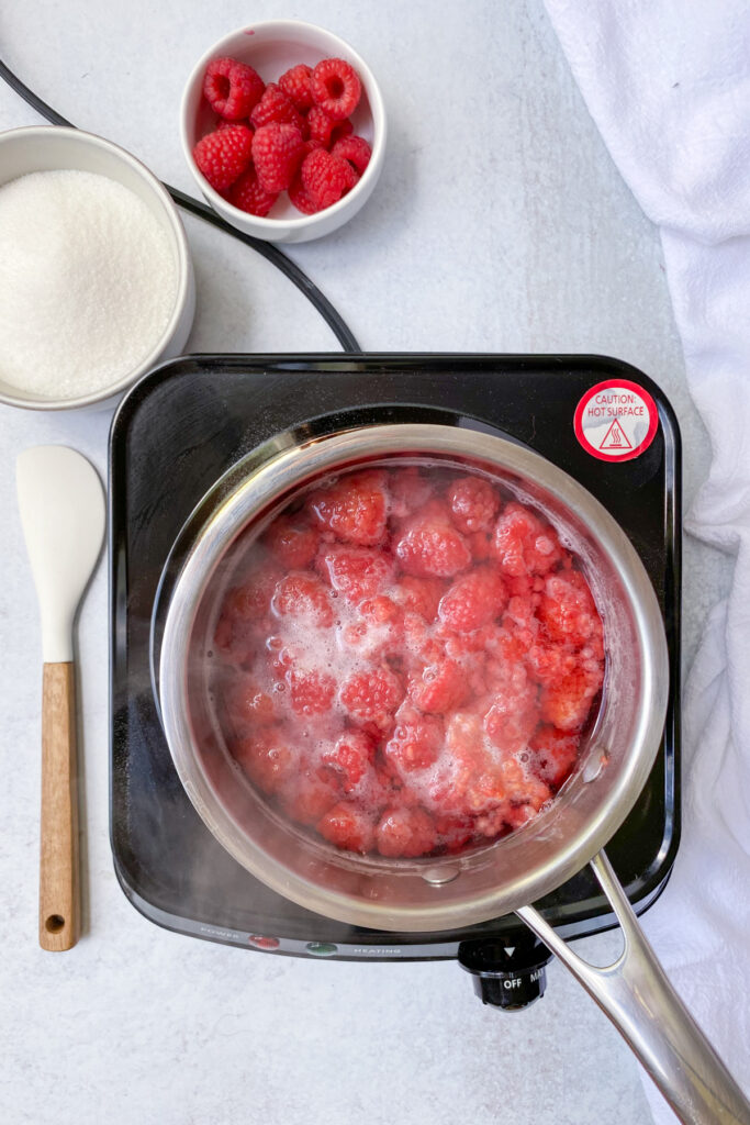 Simmering raspberries and water in a saucepan on the stove. The berries have become pale.