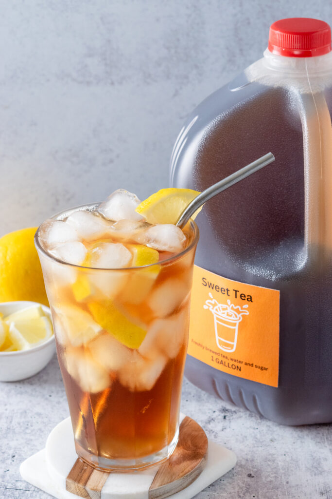 A glass full of iced sweet tea, next to a gallon pitcher of homemade tea with a sweet tea label on it.