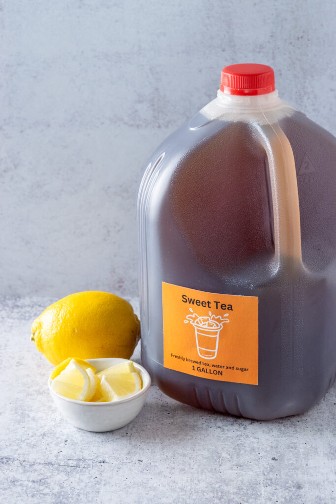 A gallon of homemade sweet tea in a gallon jug next to a lemon and bowl of lemon wedges.