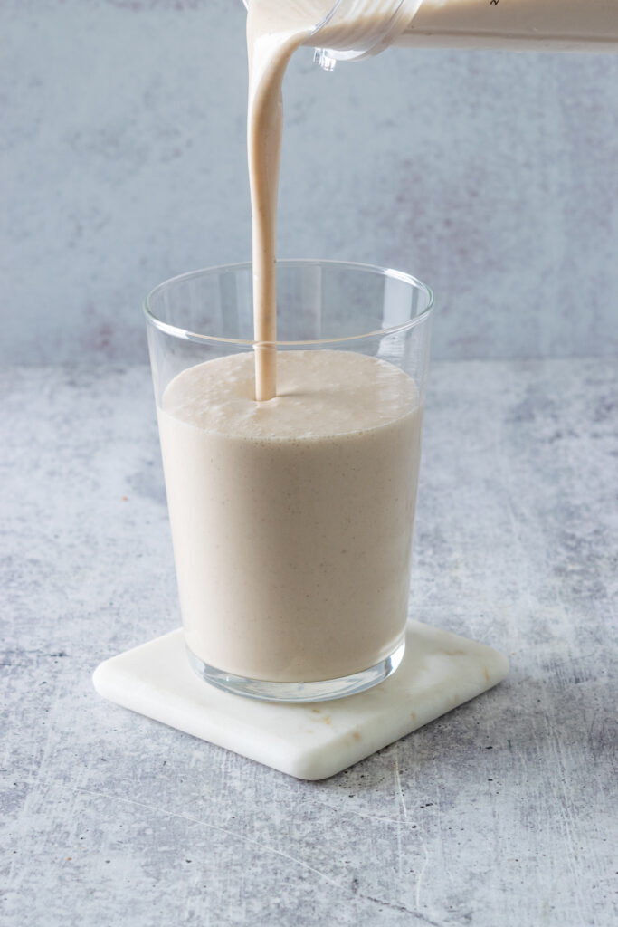 Banana chai smoothie being poured from the blender container into a clear glass for drinking.