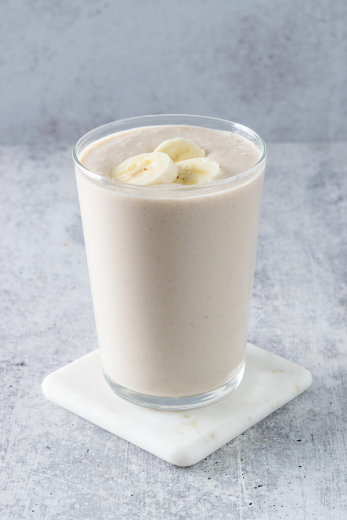 A homemade chai banana smoothie topped with three slices of banana in a clear glass that's sitting on a white, marble coaster.