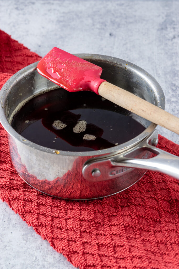 The syrup at a low boil in a saucepan with a red rubber spatula resting on top.