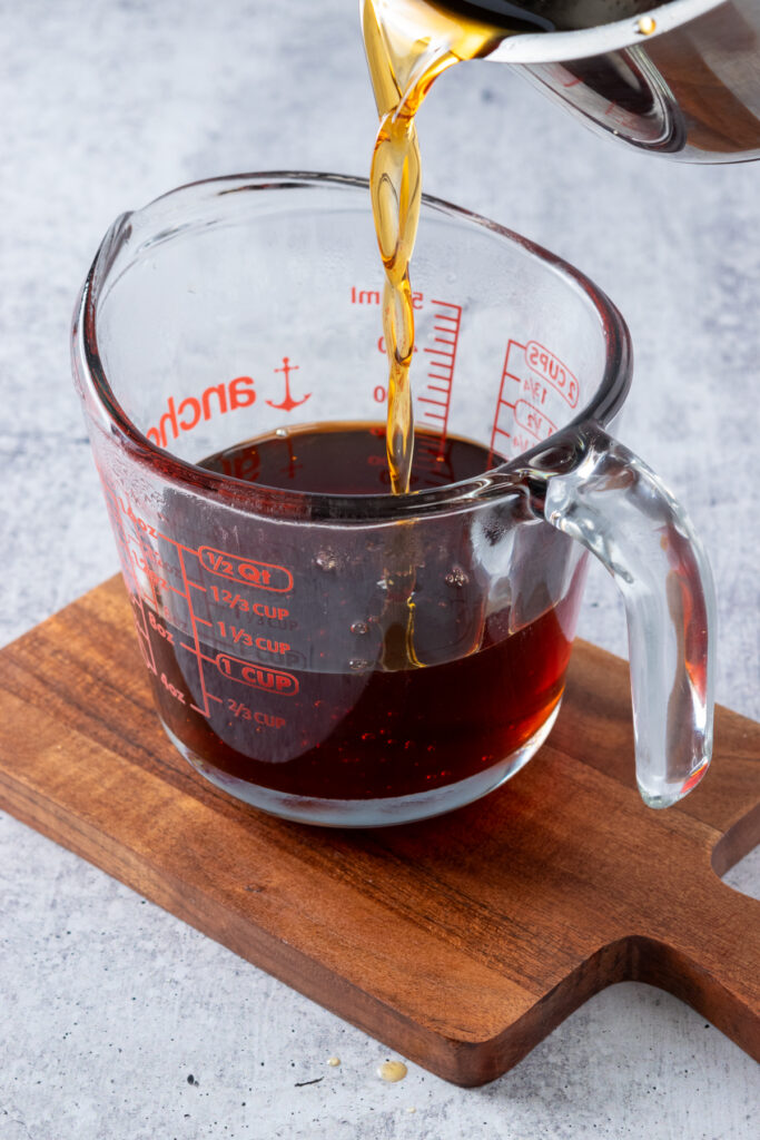 The syrup being poured from the saucepan into a glass measuring cup to show how much the recipe makes.