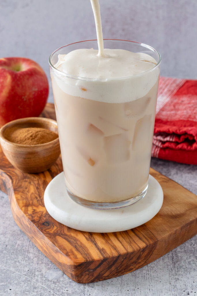 Homemade apple crisp cream cold foam being poured on top of the iced chai latte.