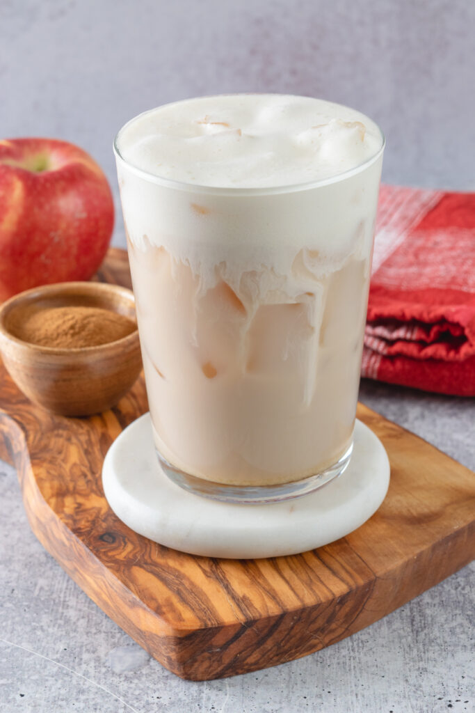 A homemade apple crisp cream chai in a clear glass that shows the chai latte with a thick layer of creamy apple foam on top.