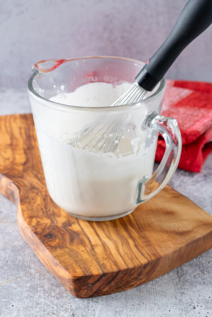 A glass Pyrex measuring cup that is frosty and has heavy cream in it that's been whisked so it's thick.