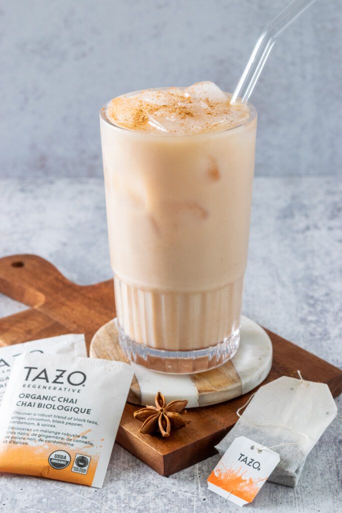 Homemade iced chai tea latte in a tall glass on a coaster, next to some chai tea bags.