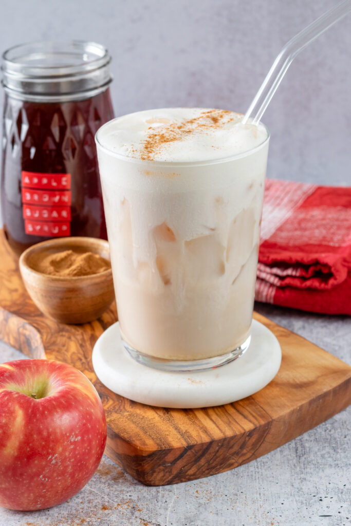 A Starbucks copycat Iced Apple Crisp Cream Chai next to a bottle of homemade apple brown sugar syrup.