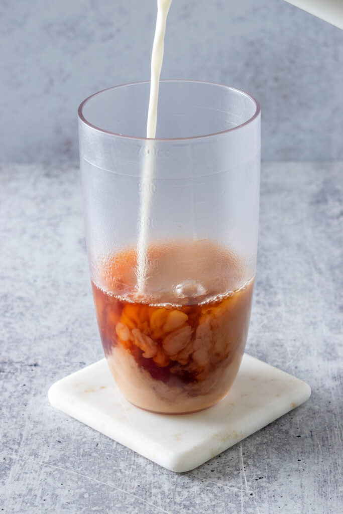 Milk being poured into a drink shaker that has concentrated chai tea in it.