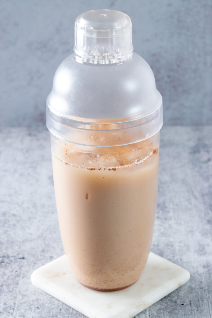 A drink shaker with ice and a chai tea latte that has been shaken to cool it down.