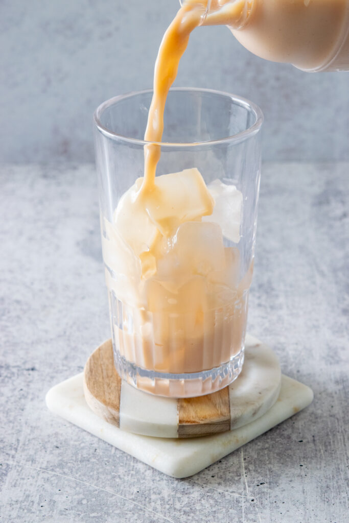 Pouring the iced chai tea latte out of the shaker through a strainer into a glass that's filled with fresh ice cubes.