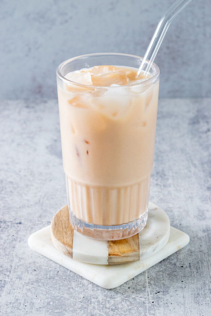 A glass filled with ice and a homemade iced chai tea latte with a glass straw in it.