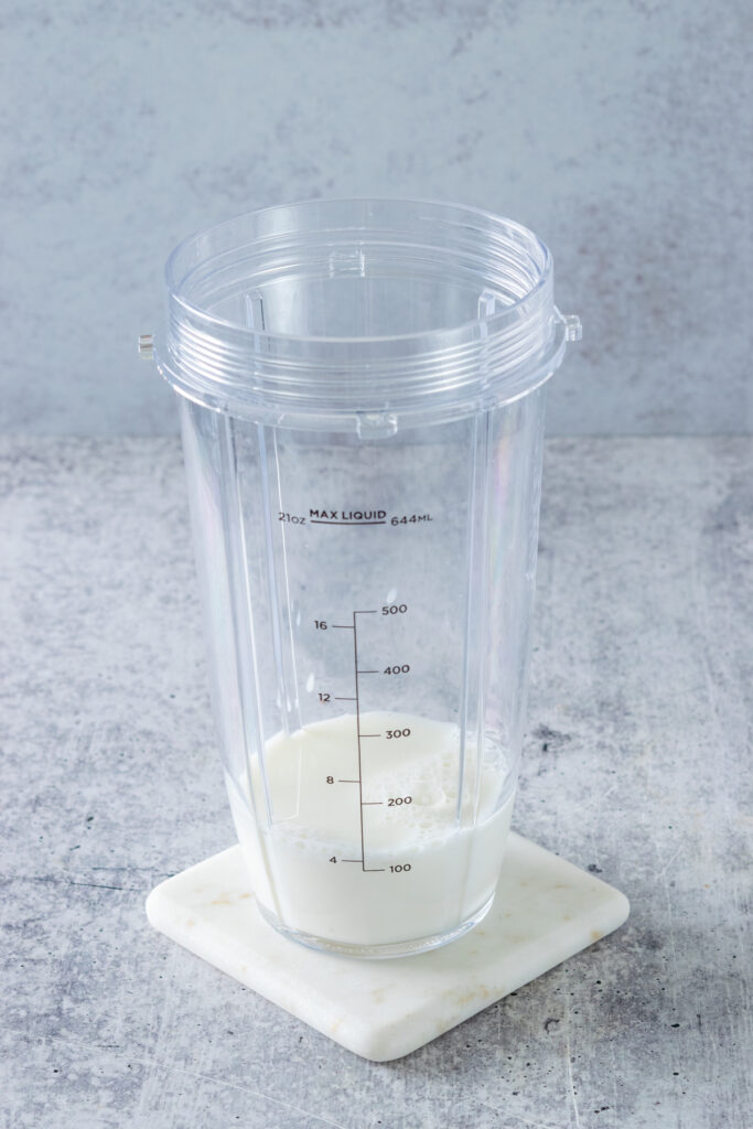 A blender cup sitting on a white coaster with milk poured into  it.