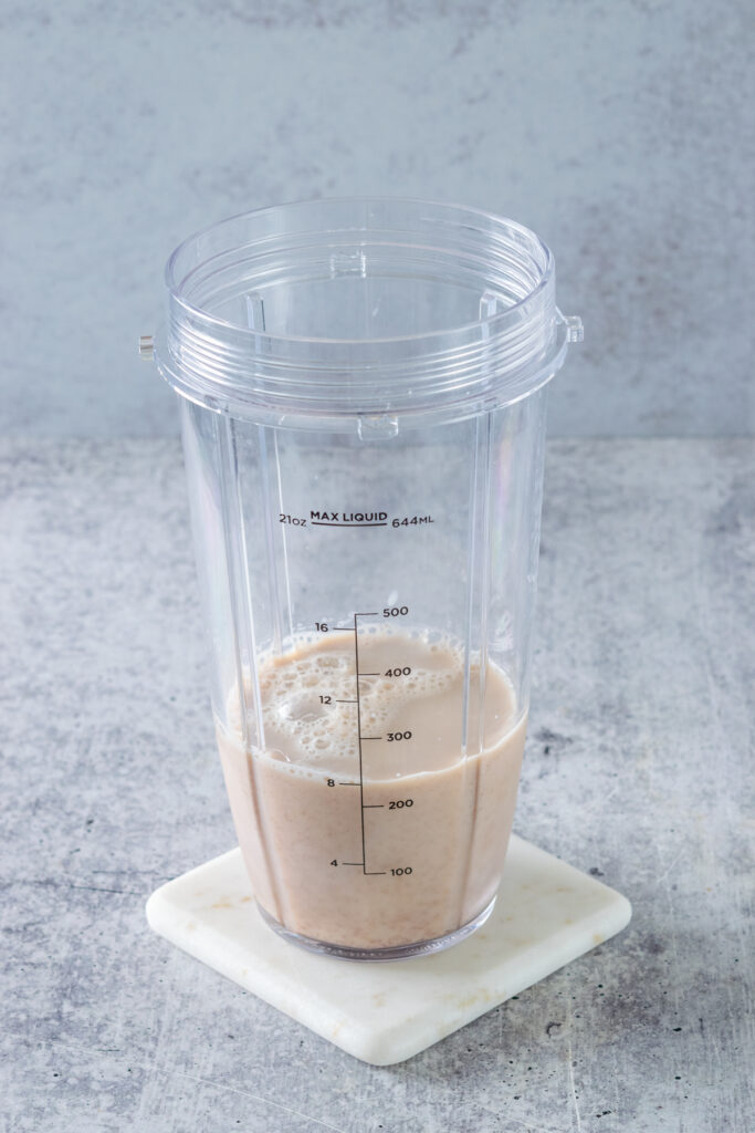 A blender cup sitting on a white coaster with milk and chai tea combined in it.