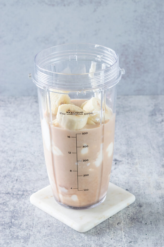 Frozen banana chunks added to a blender cup with milk, chai and yogurt to make a banana chai smoothie.