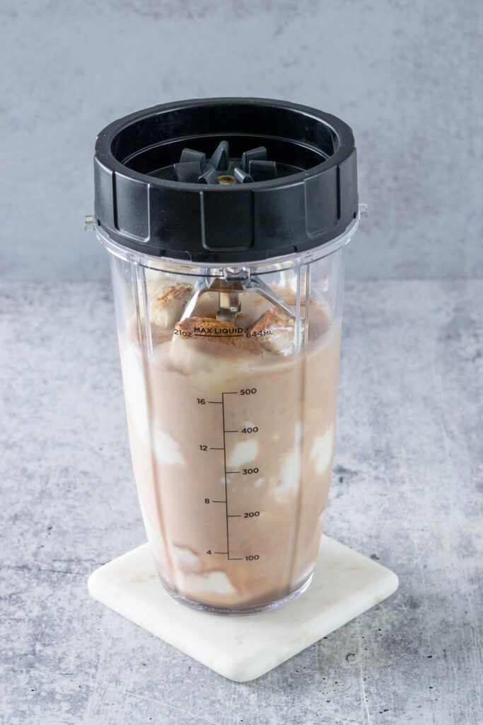 A lid with blades screwed onto a blender cup that has chai tea latte, yogurt, chunks of banana and cinnamon in it.