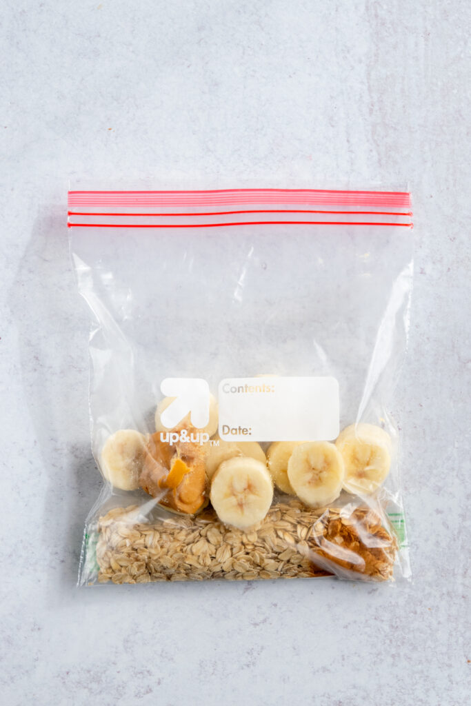 A banana oatmeal smoothie freezer pack, which is a baggie that contains pre-measured ingredients, including, oats and dry ingredients, frozen banana chunks, and a frozen scoop of peanut butter.