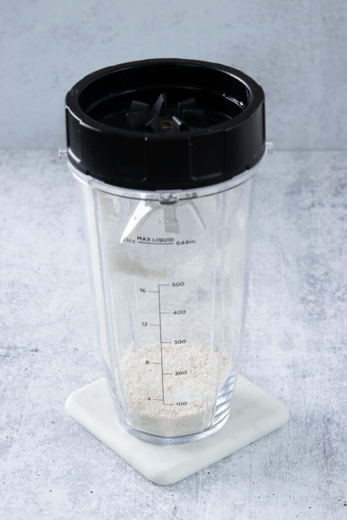 Oats that have been blended and turned into powder, in a blender cup with the lid on top.