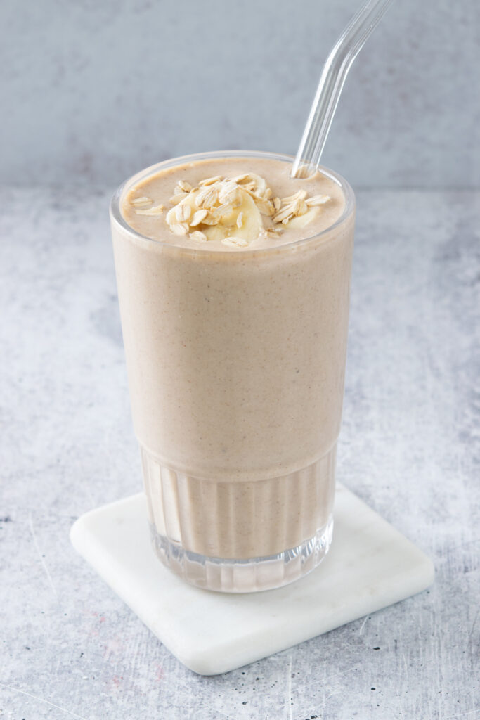 A banana oatmeal smoothie in a glass with straw, garnished with slices of banana and oats, and ready to drink.