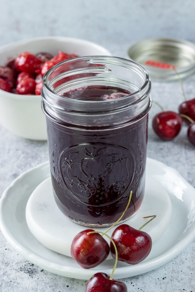 Jar of homemade cherry syrup next to a bowl of cherries.