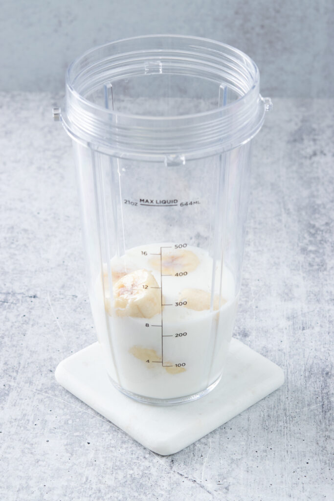 Blender cup with milk and chunks of banana in it.