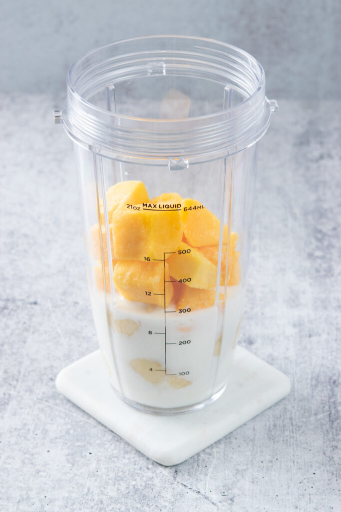 Blender cup with milk, chunks of banana and frozen mango in it.