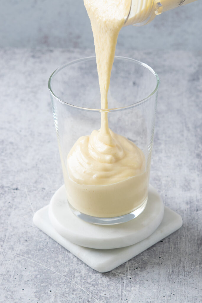 Homemade mango banana smoothie being poured into a drinking glass.