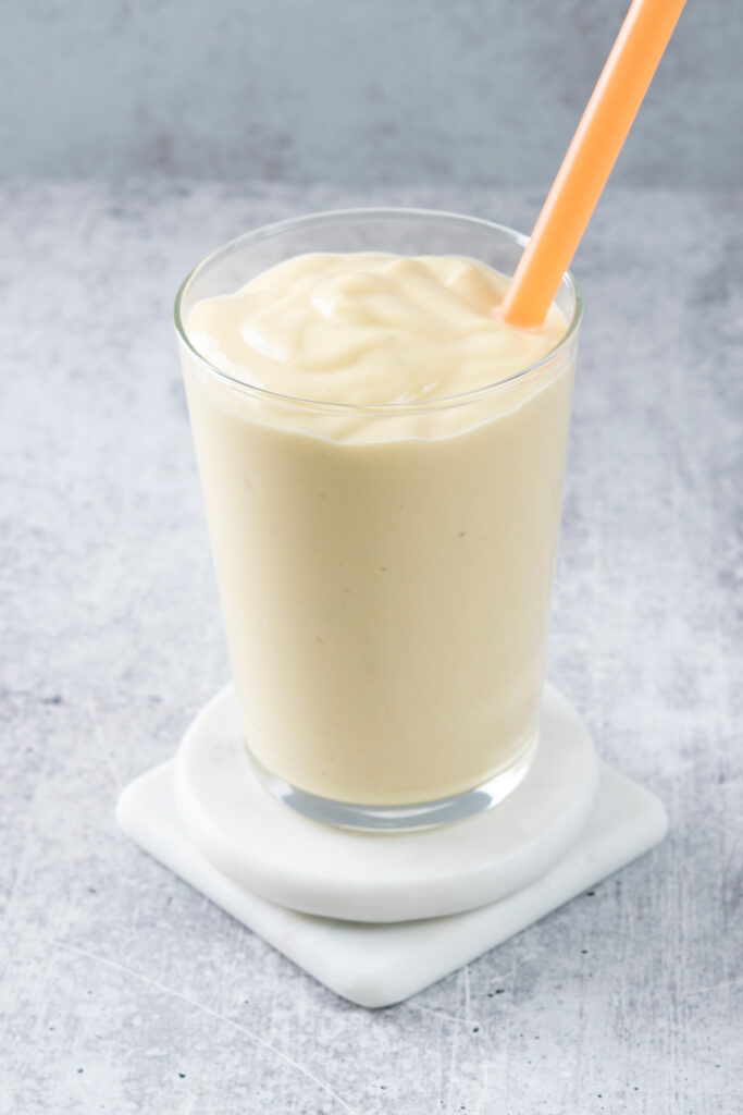 A freshly poured mango banana smoothie in a glass with an orange straw in it.