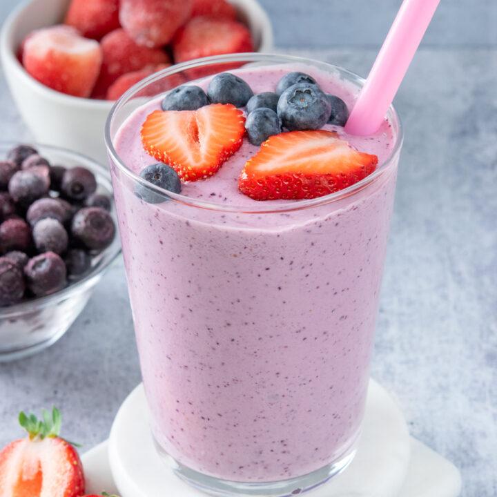 A blended strawberry blueberry smoothie in a glass with a pink straw. The smoothie is garnished with fresh blueberries and strawberries.