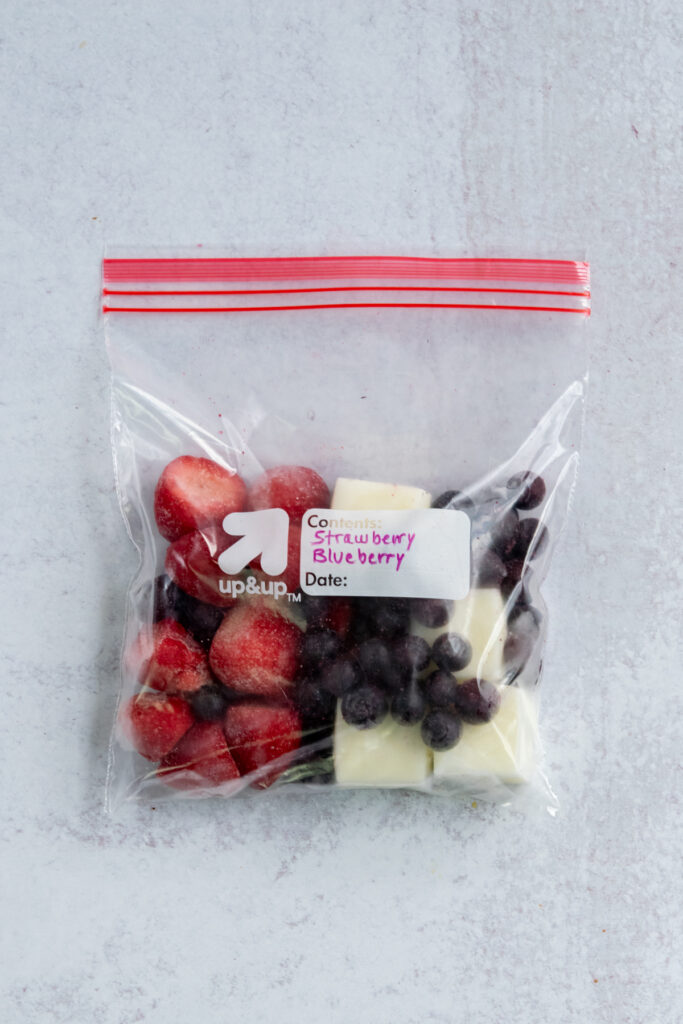 A DIY strawberry blueberry freezer pack. The plastic bag is filled with frozen fruit and a few cubes of frozen Greek yogurt.