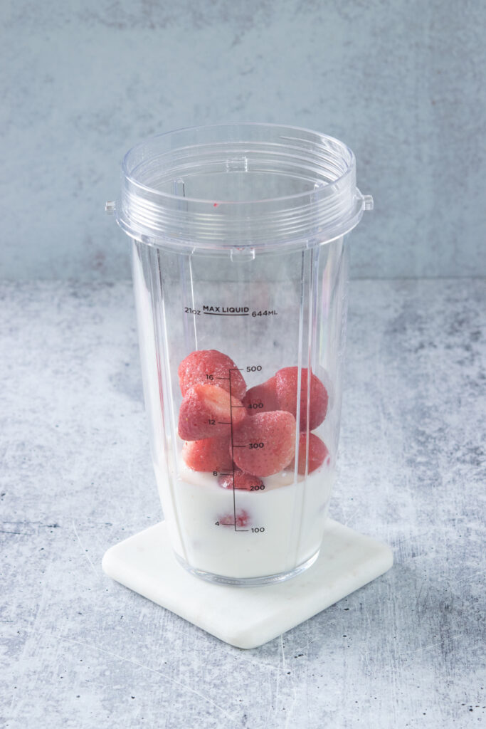 A blender cup that has milk and frozen strawberries in it.