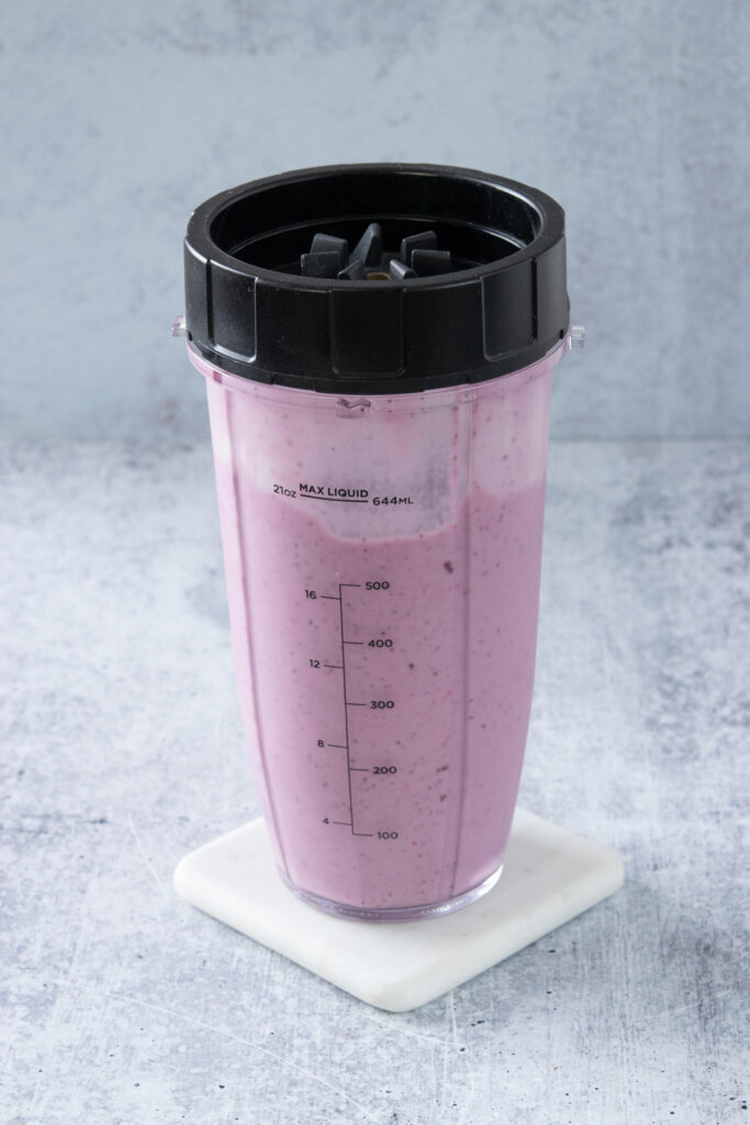 A blended strawberry blueberry smoothie still in the blender cup with the screw top lid and blade on it.