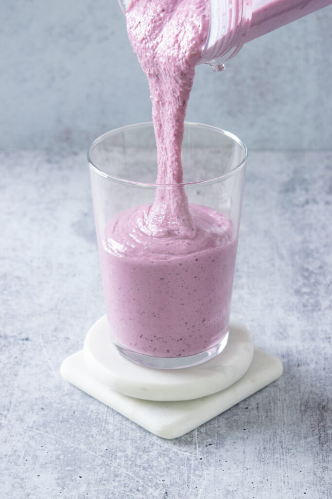 The thick, purple-colored blended strawberry blueberry fruit smoothie being poured into a cup.