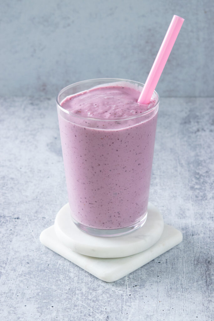 A homemade strawberry blueberry smoothie that blended into a pretty purple color, filled in a glass with a pink straw in it.