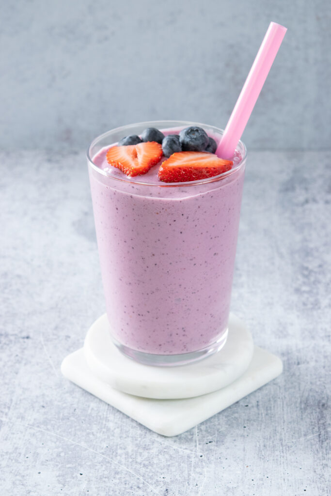 A smoothie garnished with fresh strawberries and blueberries on top.