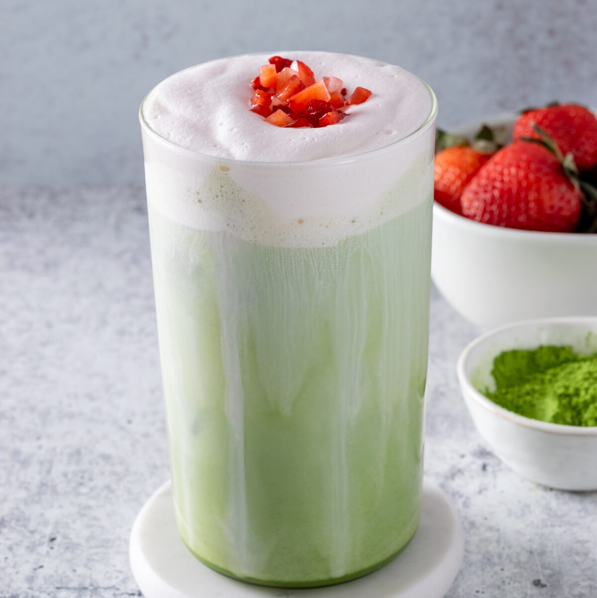 Navigation image for matcha green tea drink recipes, showing an iced matcha latte topped with sweet cream cold foam and chopped strawberries.